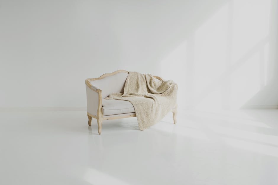 A close-up image of two vintage upholstered armchairs situated on a light-colored wooden floor inside a room, which appears to be undergoing cleaning or maintenance. The chair on the left features a w